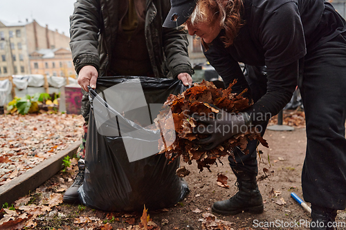 Image of Father-daughter duo bonding in the garden as they work together to collect fallen leaves and fill up a bag on a crisp autumn day.