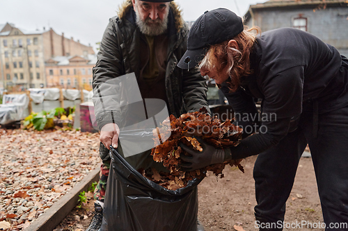 Image of Father-daughter duo bonding in the garden as they work together to collect fallen leaves and fill up a bag on a crisp autumn day.