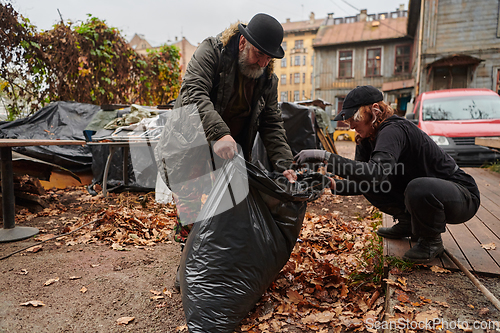 Image of Father-daughter duo bonding in the garden as they work together to collect fallen leaves and fill up a bag on a crisp autumn day.