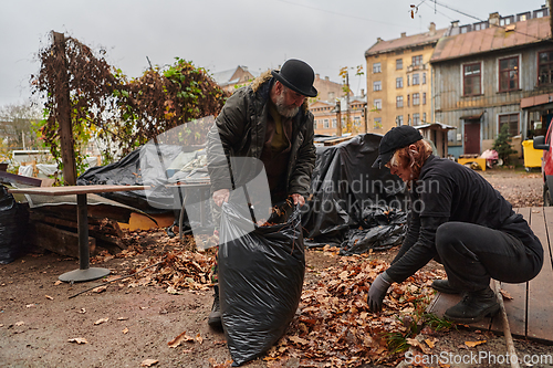 Image of Father-daughter duo bonding in the garden as they work together to collect fallen leaves and fill up a bag on a crisp autumn day.