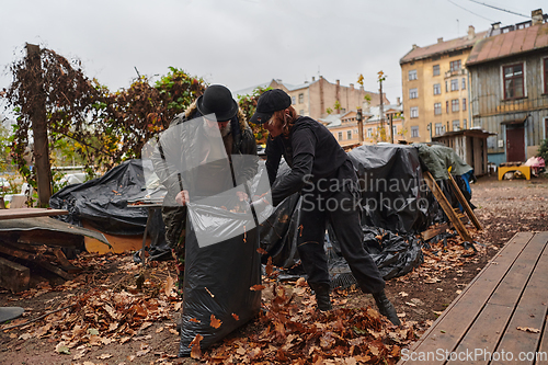 Image of Father-daughter duo bonding in the garden as they work together to collect fallen leaves and fill up a bag on a crisp autumn day.