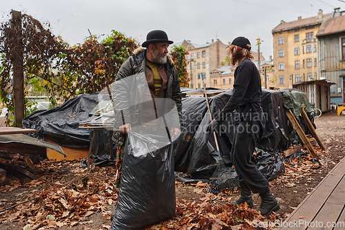 Image of Father-daughter duo bonding in the garden as they work together to collect fallen leaves and fill up a bag on a crisp autumn day.