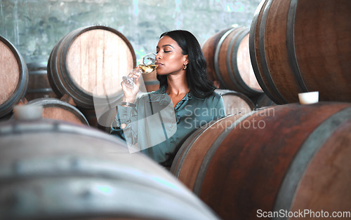 Image of Woman doing wine tasting, drinking glass of chardonnay or sauvignon blanc in winery cellar amongst barrels on vineyard. Beautiful oenologist or sommelier enjoying a relaxing, luxury beverage indoors.