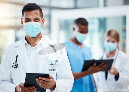 Image of A successful male doctor browsing the internet, using a tablet and wearing a mask inside a hospital. Portrait of a healthcare professional searching covid, flu or disease on a digital device