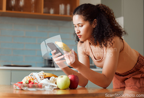 Image of Woman reading phone, researching a diet with fresh fruit while relaxing in a kitchen at home. Young female searching for a recipe, cleanse or detox online. Lady checking nutritional value of a banana