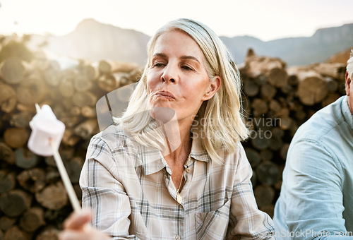 Image of Senior woman eating marshmallow with regret, relaxing by the campfire after her mountain adventure in the outdoors nature. Female enjoying wellness lifestyle, resting after hiking trip with friends