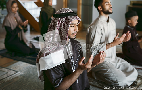 Image of Young muslim family pray together, sit on knees at home practicing Islam. Religious women wearing hijab and spiritual men wear traditional attire, close eyes and concentrate on prayer with hands up.