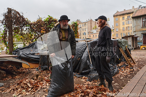 Image of Father-daughter duo bonding in the garden as they work together to collect fallen leaves and fill up a bag on a crisp autumn day.