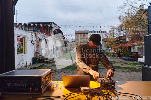 Image of A young man is entertaining a group of friends in the backyard of his house, becoming their DJ and playing music in a casual outdoor gathering