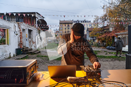 Image of A young man is entertaining a group of friends in the backyard of his house, becoming their DJ and playing music in a casual outdoor gathering