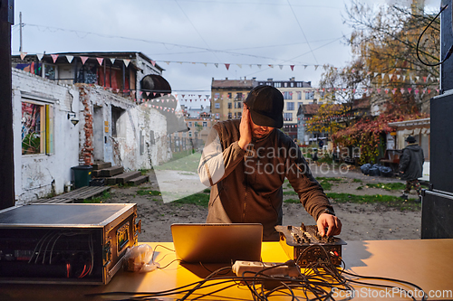 Image of A young man is entertaining a group of friends in the backyard of his house, becoming their DJ and playing music in a casual outdoor gathering