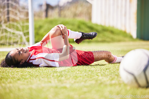 Image of Injured, pain or injury of a female soccer player lying on a field holding her knee during a match. Hurt woman footballer with a painful leg on the ground in agony having a bad day on the pitch