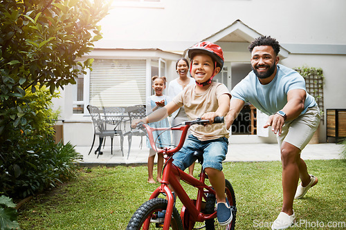 Image of Learning, bicycle and proud dad teaching his young son to ride while wearing a helmet for safety in their family home garden. Active father helping and supporting his child while cycling outside