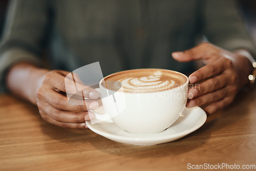 Image of Woman drinking coffee, sitting and relaxing in a cafe. Close up of an African lady with cappuccino, holding a cup at a restaurant table. Enjoying a hot beverage while on a break, taking time for rest