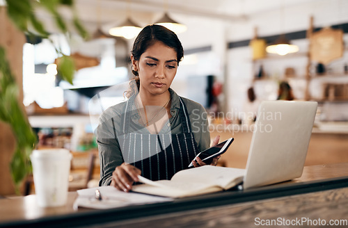 Image of Cafe owner with laptop, phone and book checking online order, searching available bookings and preparing takeaway deliveries coffee shop. Serious local restaurant entrepreneur pricing a menu on tech