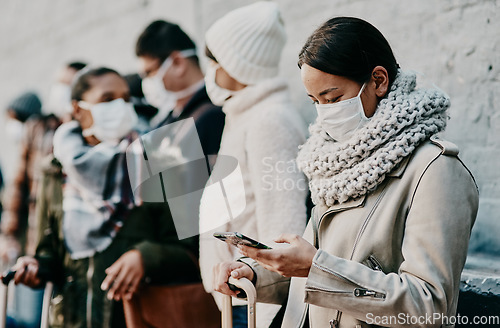 Image of People or tourists traveling during covid and standing in line at a public travel facility wearing protective masks. Woman in a queue reading social media news about coronavirus pandemic on her phone