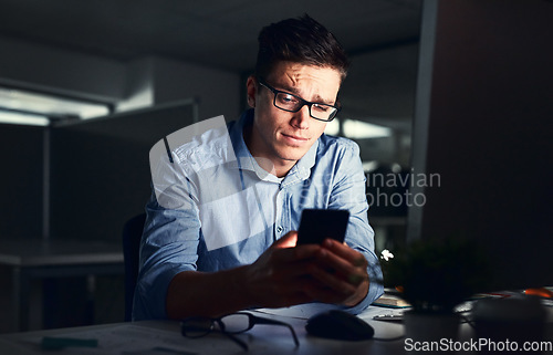 Image of Confused businessman texting on his phone at the office at night. Handsome, confident and corporate caucasian male looking at messages from coworkers while working overtime and feeling unsure