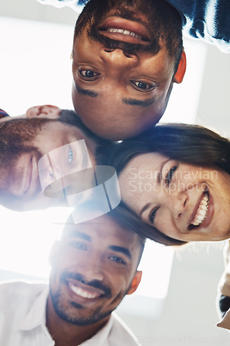 Image of Portrait of a diverse group of happy office workers from below joining together in a huddle for support and unity with lights in the background. Cheerful motivated colleagues ready for business