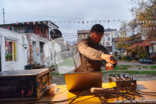 Image of A young man is entertaining a group of friends in the backyard of his house, becoming their DJ and playing music in a casual outdoor gathering