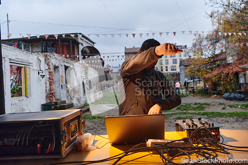 Image of A young man is entertaining a group of friends in the backyard of his house, becoming their DJ and playing music in a casual outdoor gathering