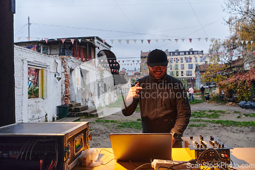 Image of A young man is entertaining a group of friends in the backyard of his house, becoming their DJ and playing music in a casual outdoor gathering