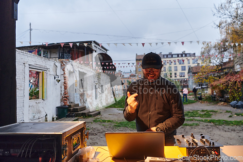 Image of A young man is entertaining a group of friends in the backyard of his house, becoming their DJ and playing music in a casual outdoor gathering