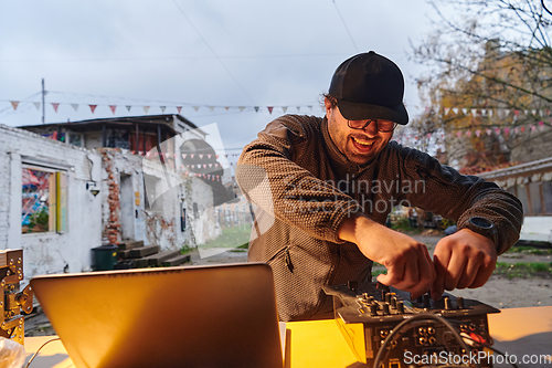 Image of A young man is entertaining a group of friends in the backyard of his house, becoming their DJ and playing music in a casual outdoor gathering