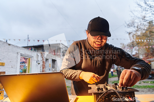 Image of A young man is entertaining a group of friends in the backyard of his house, becoming their DJ and playing music in a casual outdoor gathering