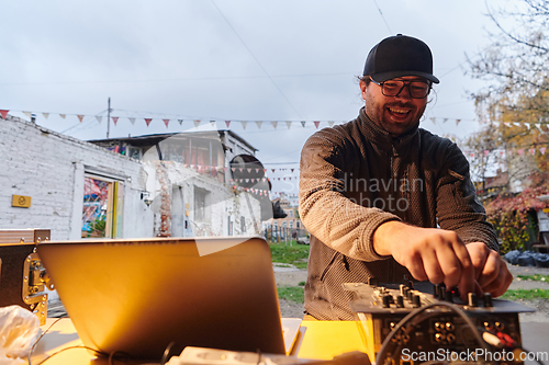 Image of A young man is entertaining a group of friends in the backyard of his house, becoming their DJ and playing music in a casual outdoor gathering