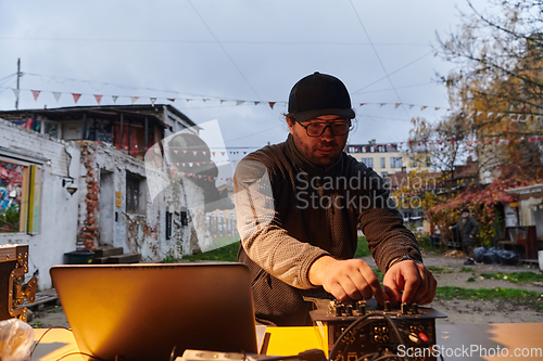 Image of A young man is entertaining a group of friends in the backyard of his house, becoming their DJ and playing music in a casual outdoor gathering