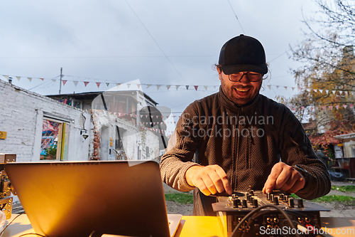 Image of A young man is entertaining a group of friends in the backyard of his house, becoming their DJ and playing music in a casual outdoor gathering