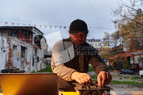 Image of A young man is entertaining a group of friends in the backyard of his house, becoming their DJ and playing music in a casual outdoor gathering