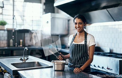 Image of Cooking, making food and working as a chef in a commercial kitchen with tongs and industrial equipment. Portrait of a female cook preparing a meal for lunch, dinner or supper in a restaurant or cafe