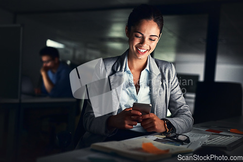 Image of Woman reading text late on phone, smiling at a message and looking at social media posts online while working in a dark office at night. Happy corporate worker checking emails and doing overtime