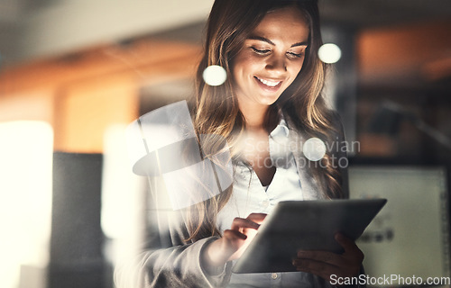 Image of Working late, overtime and dedication with a happy, positive and motivated business woman working on a tablet in her office. Young female executive smiling while feeling dedicated and determined