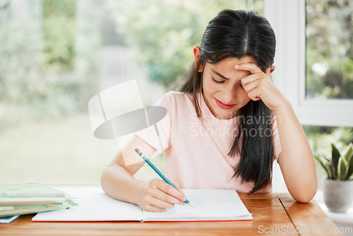 Image of Stressed, frustrated and unhappy girl writing homework with a difficult task alone at home. Tired school child studying for a hard exam. Upset student learning with homeschooling education.