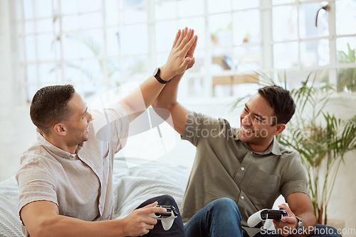 Image of Men high five, celebrate and enjoy playing video games in the sofa at home. Happy, cheerful and best friends having fun and winning while holding wireless controllers with live online game