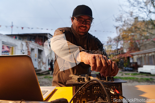 Image of A young man is entertaining a group of friends in the backyard of his house, becoming their DJ and playing music in a casual outdoor gathering