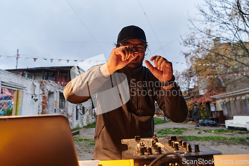 Image of A young man is entertaining a group of friends in the backyard of his house, becoming their DJ and playing music in a casual outdoor gathering