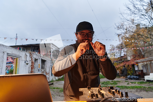 Image of A young man is entertaining a group of friends in the backyard of his house, becoming their DJ and playing music in a casual outdoor gathering