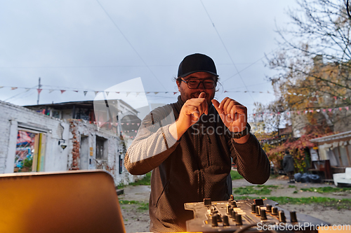 Image of A young man is entertaining a group of friends in the backyard of his house, becoming their DJ and playing music in a casual outdoor gathering