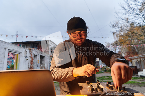 Image of A young man is entertaining a group of friends in the backyard of his house, becoming their DJ and playing music in a casual outdoor gathering