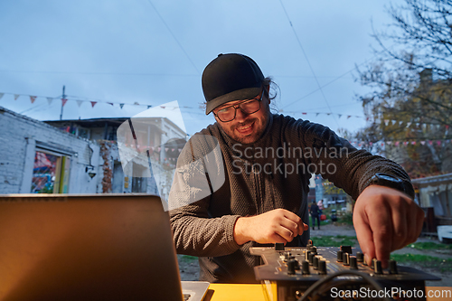 Image of A young man is entertaining a group of friends in the backyard of his house, becoming their DJ and playing music in a casual outdoor gathering