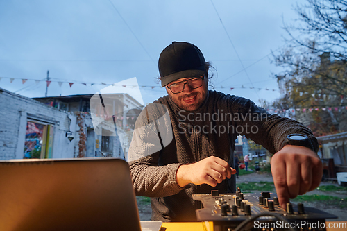 Image of A young man is entertaining a group of friends in the backyard of his house, becoming their DJ and playing music in a casual outdoor gathering