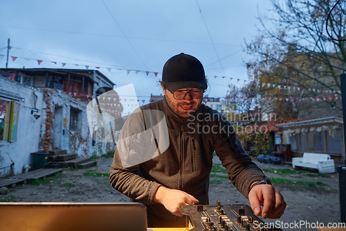 Image of A young man is entertaining a group of friends in the backyard of his house, becoming their DJ and playing music in a casual outdoor gathering