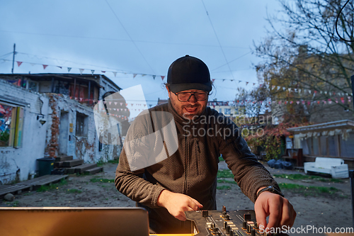 Image of A young man is entertaining a group of friends in the backyard of his house, becoming their DJ and playing music in a casual outdoor gathering