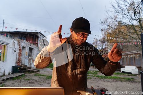 Image of A young man is entertaining a group of friends in the backyard of his house, becoming their DJ and playing music in a casual outdoor gathering