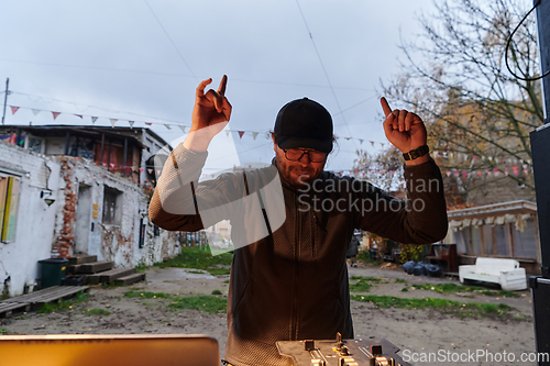 Image of A young man is entertaining a group of friends in the backyard of his house, becoming their DJ and playing music in a casual outdoor gathering