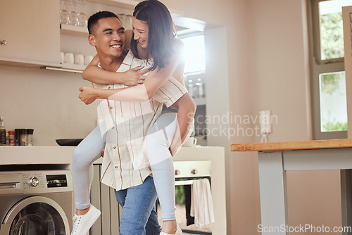 Image of Happy, playful and excited couple playing in the kitchen at home and the boyfriend giving a piggyback ride to his girlfriend. Carefree and joyful lovers having fun together and enjoying the weekend