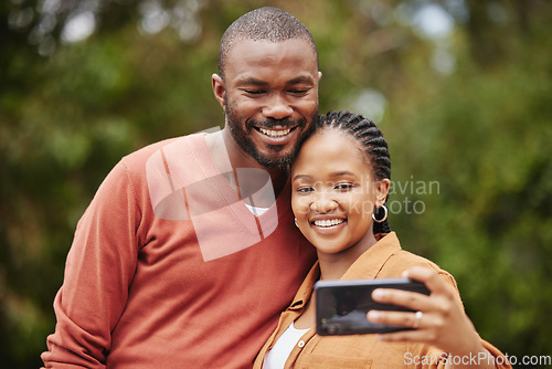 Image of Trendy, modern couple taking selfie on phone while on a romantic date in a park and sharing relationship status on social media app. Smiling, in love married husband and wife capturing happy memories